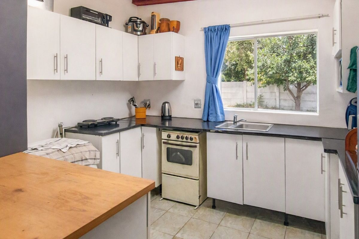 Functional kitchen featuring white cabinetry, dark laminate countertops, a stainless steel sink, and a freestanding oven with tiled flooring.
