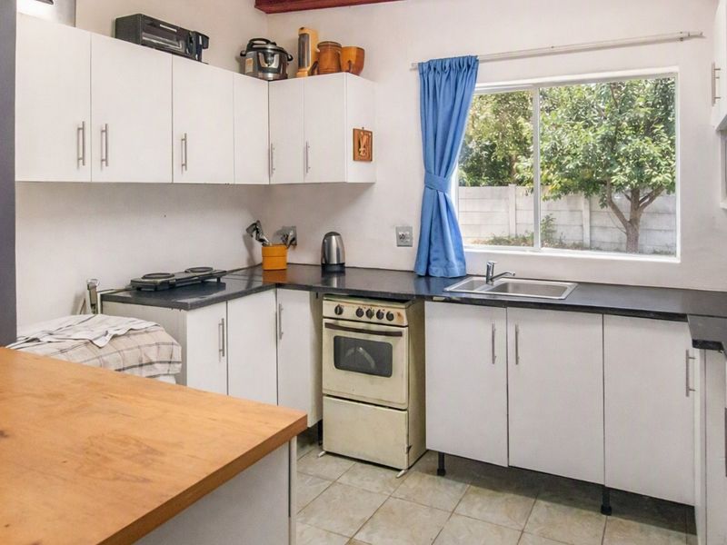 Functional kitchen featuring white cabinetry, dark laminate countertops, a stainless steel sink, and a freestanding oven with tiled flooring.