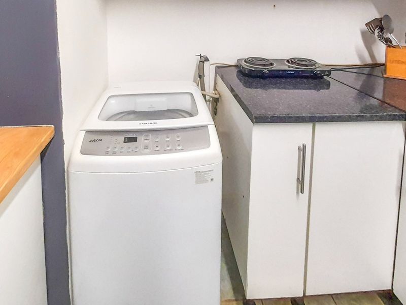 A compact scullery or utility area featuring built-in cabinetry, a stone-look countertop, and an electric hob, providing functional workspace and laundry appliance housing.