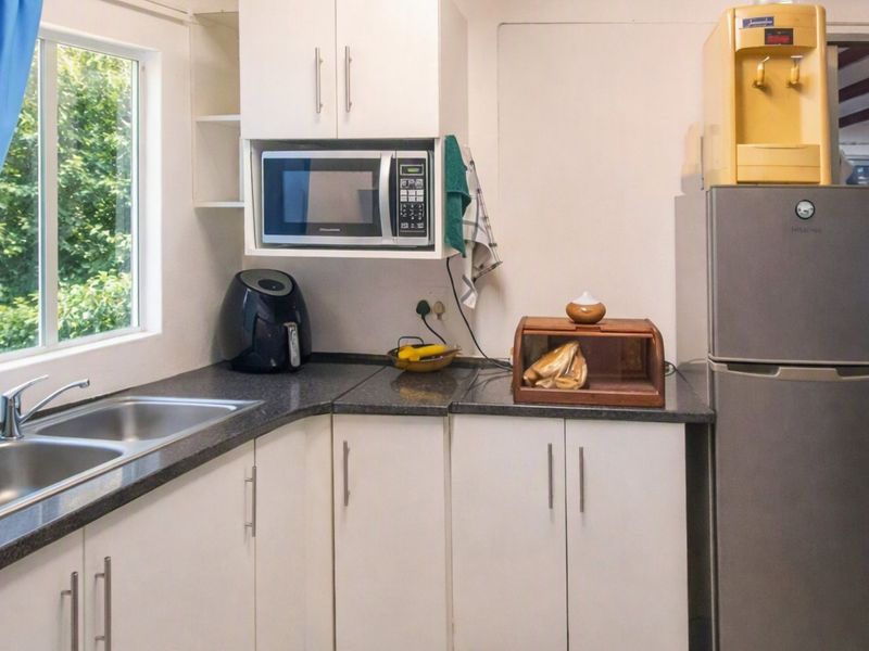 A functional kitchen area featuring white cabinetry, dark laminate countertops, and a stainless steel double sink with a window view.