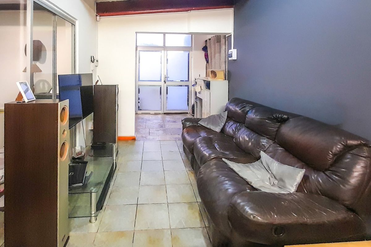 A living room featuring tiled flooring, an exposed ceiling beam, and access to an adjacent area through a glass sliding door.
