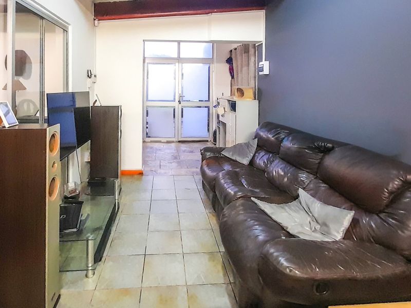 A living room featuring tiled flooring, an exposed ceiling beam, and access to an adjacent area through a glass sliding door.
