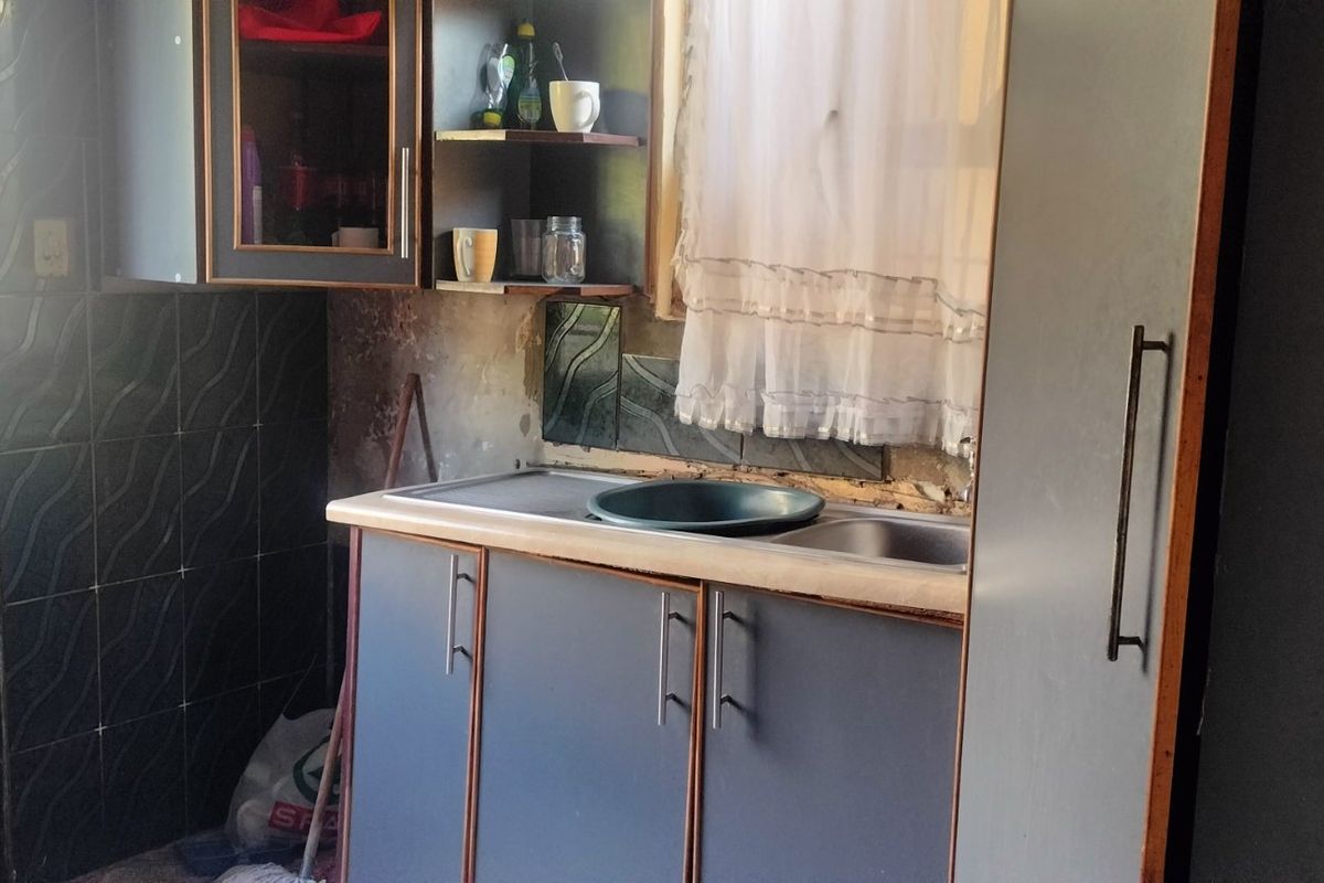 A compact kitchen area featuring built-in cabinetry, a stainless steel sink, and tiled splashback, requiring maintenance and cosmetic updates to improve functionality and appearance.