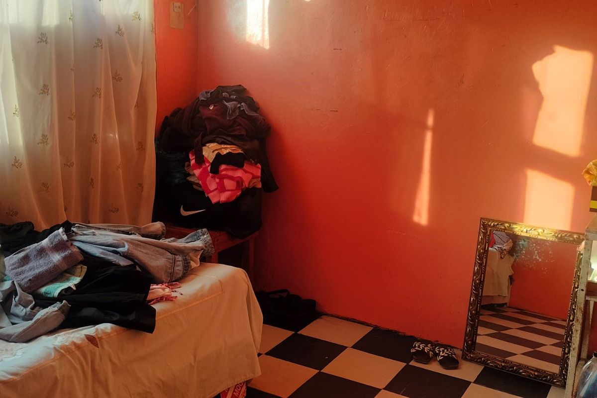 A bedroom featuring checkered floor tiles and bright orange wall paint, requiring cosmetic updates to improve the overall aesthetic.