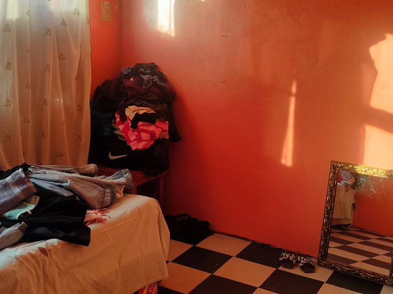 A bedroom featuring checkered floor tiles and bright orange wall paint, requiring cosmetic updates to improve the overall aesthetic.