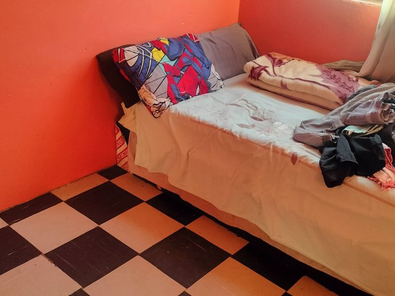 A bedroom featuring checkered vinyl flooring and bright orange wall paint, offering a functional space ready for cosmetic updates and modernization.