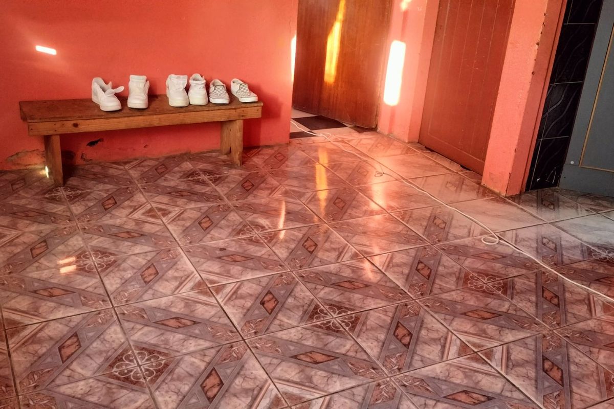 A living area featuring patterned ceramic floor tiles and orange painted walls, showing signs of wear near the baseboards.