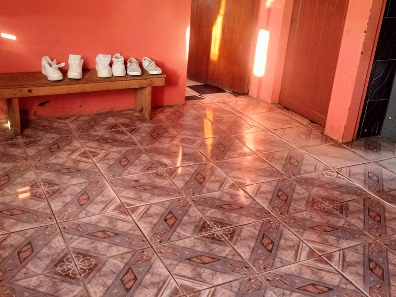 A living area featuring patterned ceramic floor tiles and orange painted walls, showing signs of wear near the baseboards.