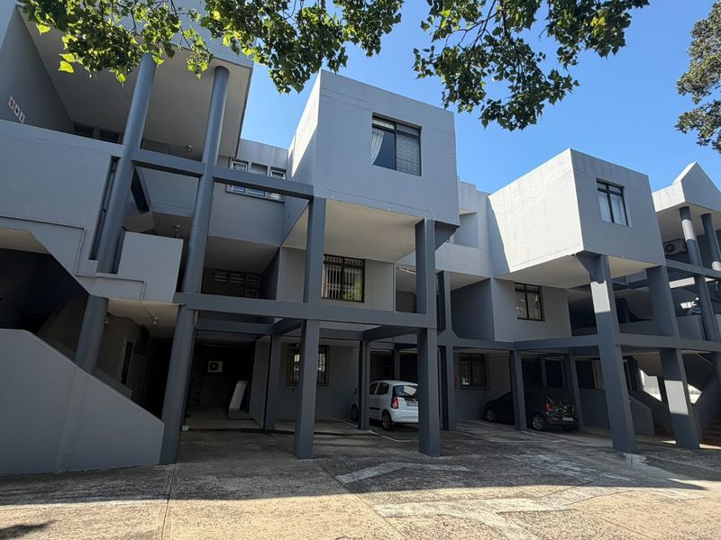 Exterior view of a multi-story apartment building featuring covered ground-level parking, concrete structural pillars, and external staircases.