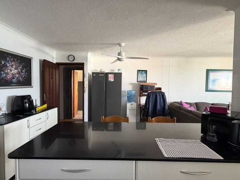 An open-plan living and kitchen area featuring a central island with a black granite countertop and white cabinetry, complemented by a ceiling fan.