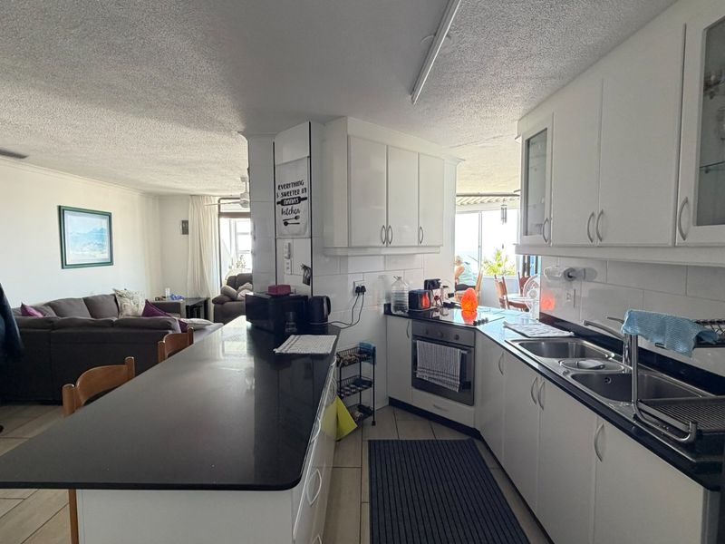 Open-plan kitchen and living area featuring white cabinetry, black granite countertops, integrated oven, and tiled flooring, creating a functional and connected living space.