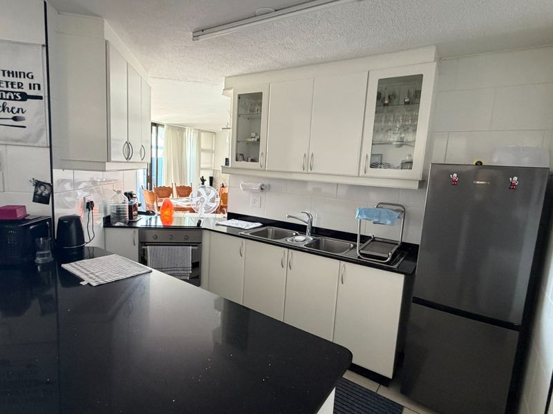 A functional kitchen featuring white cabinetry, black granite countertops, a double sink, and built-in oven, with an open-plan layout leading to the dining area.