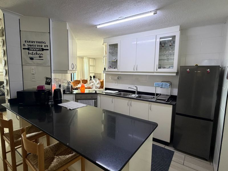 Open plan kitchen featuring black granite countertops, white cabinetry, and integrated appliances, seamlessly flowing into the adjacent living and dining areas.