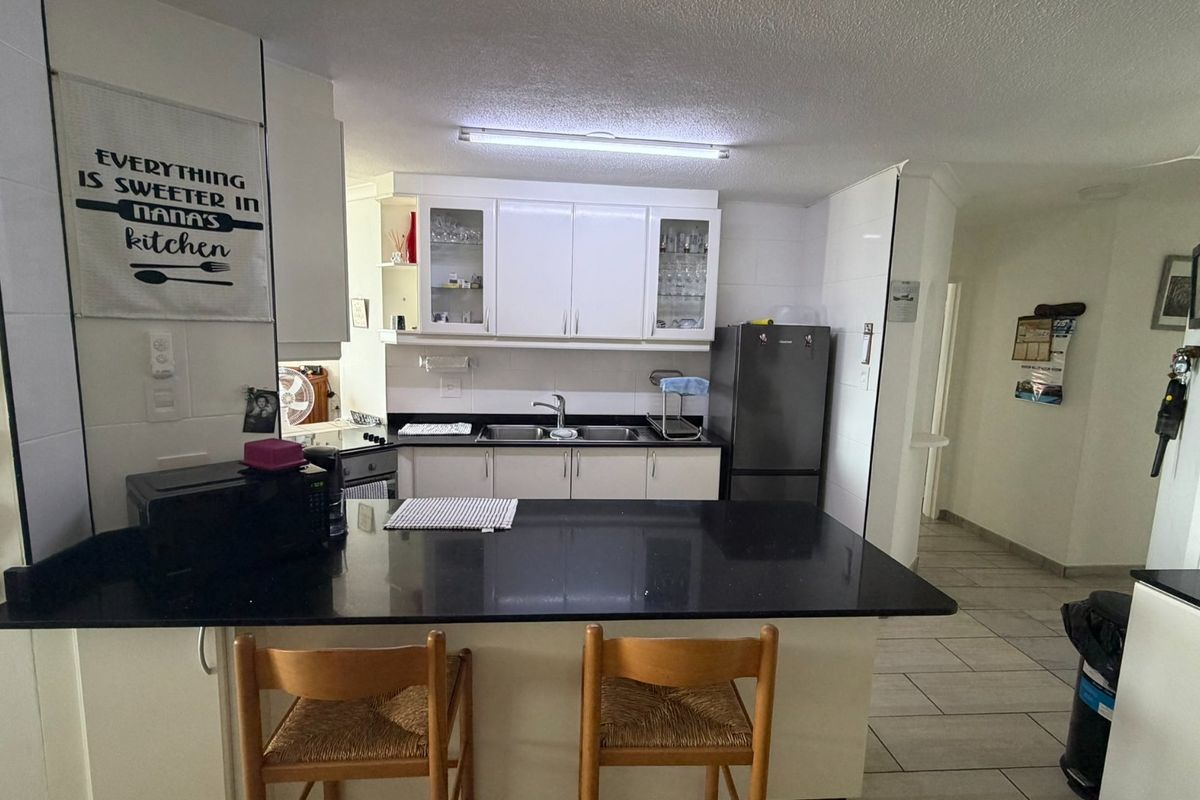 A functional kitchen featuring white cabinetry, black granite countertops, a double basin sink, and tiled flooring, offering a clean and practical workspace.