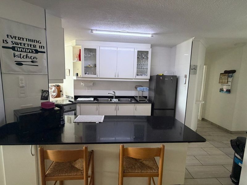 A functional kitchen featuring white cabinetry, black granite countertops, a double basin sink, and tiled flooring, offering a clean and practical workspace.