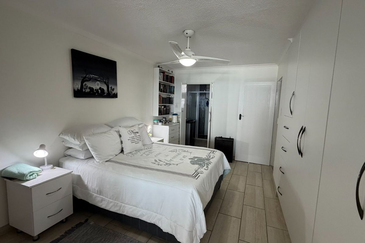 A well-maintained bedroom featuring built-in cupboards, tiled flooring, a ceiling fan, and direct access to an en-suite bathroom.