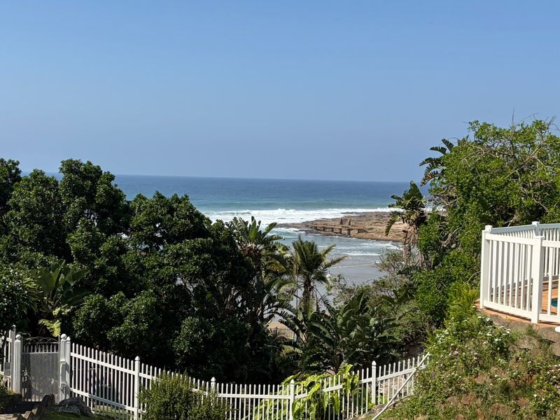 A scenic elevated view overlooking the ocean, featuring a private swimming pool and white perimeter fencing set within a lush garden environment.