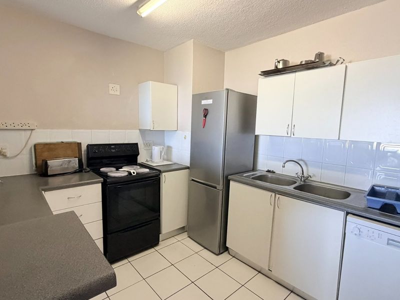 A functional kitchen featuring white cabinetry, laminate countertops, a double stainless steel sink, and tiled flooring, offering a practical layout for daily use.
