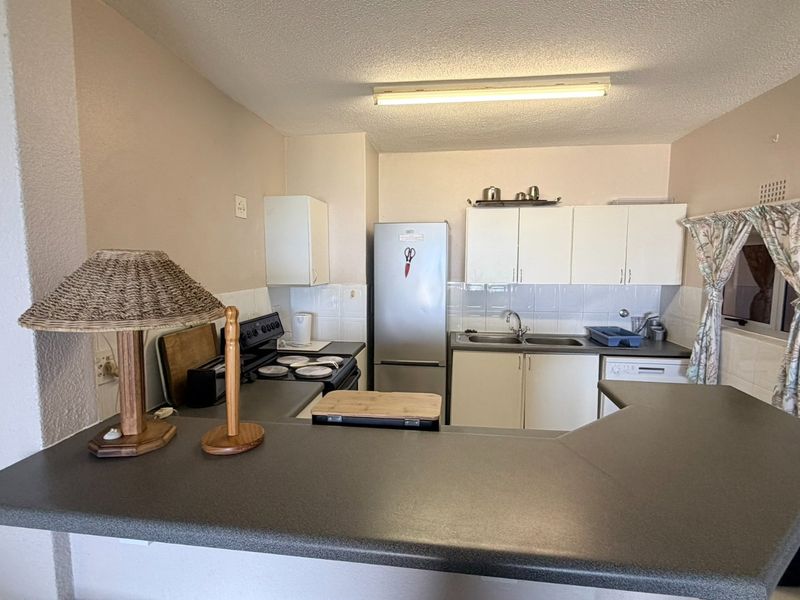 A functional kitchen featuring laminate countertops, built-in cabinetry, a tiled backsplash, and a breakfast bar overlooking the living area.