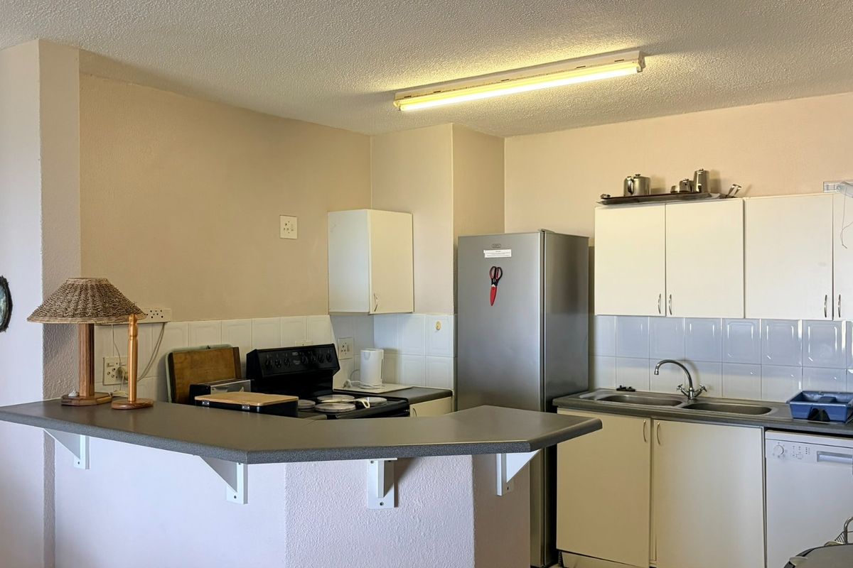 A functional kitchen featuring built-in cabinetry, a double basin sink, tiled backsplash, and a breakfast bar counter, offering potential for modern updates.