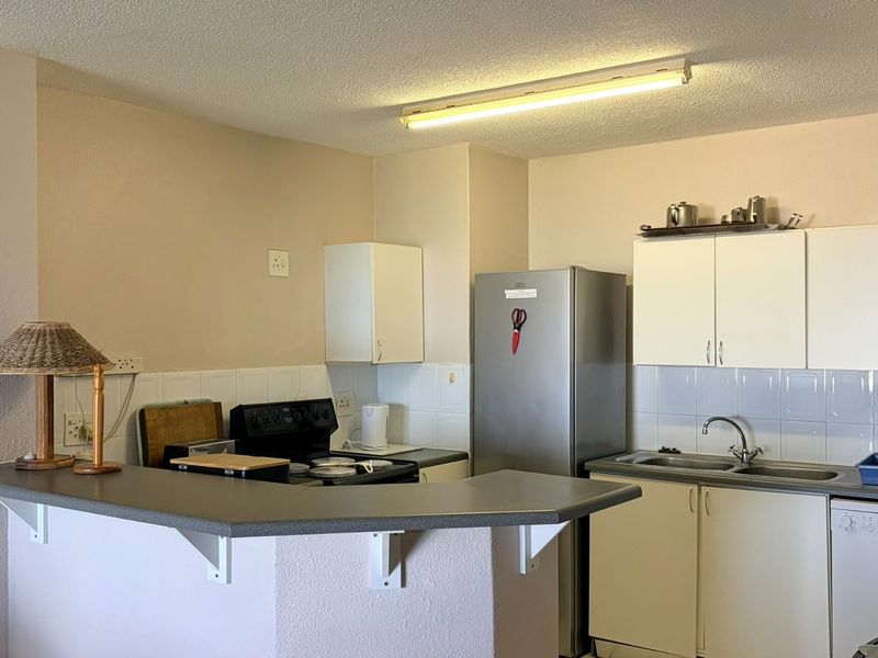 A functional kitchen featuring built-in cabinetry, a double basin sink, tiled backsplash, and a breakfast bar counter, offering potential for modern updates.