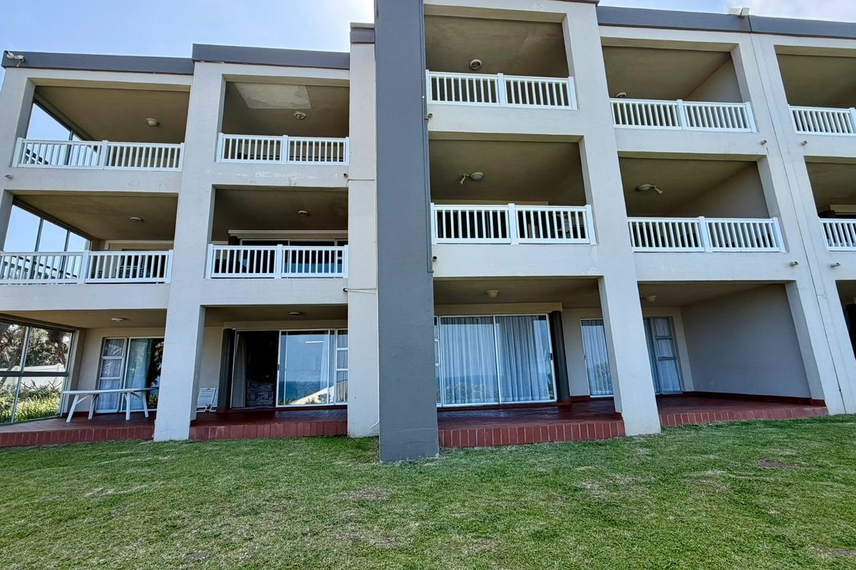 Rear view of a multi-story apartment building featuring private balconies with white railings, sliding glass doors, and ground-level tiled patio areas.