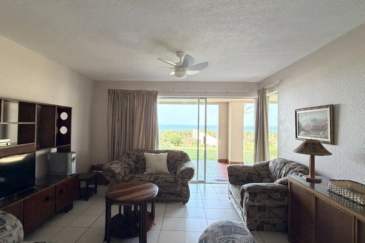 A living room featuring tiled flooring, a ceiling fan, and large sliding glass doors that open to a patio with ocean views.