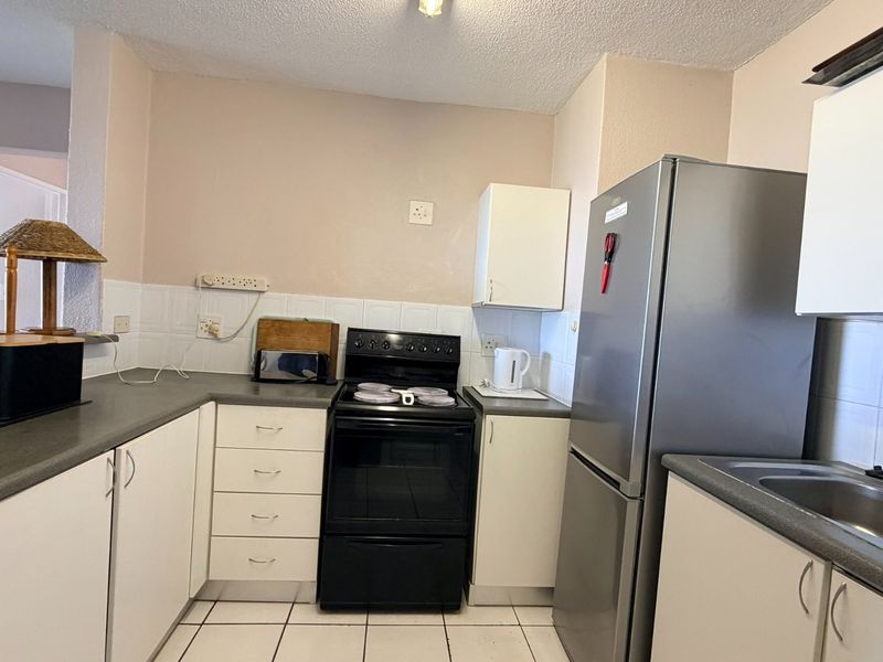 A functional kitchen featuring white cabinetry, laminate countertops, a tiled backsplash, and a freestanding stove, offering a practical layout for daily meal preparation.