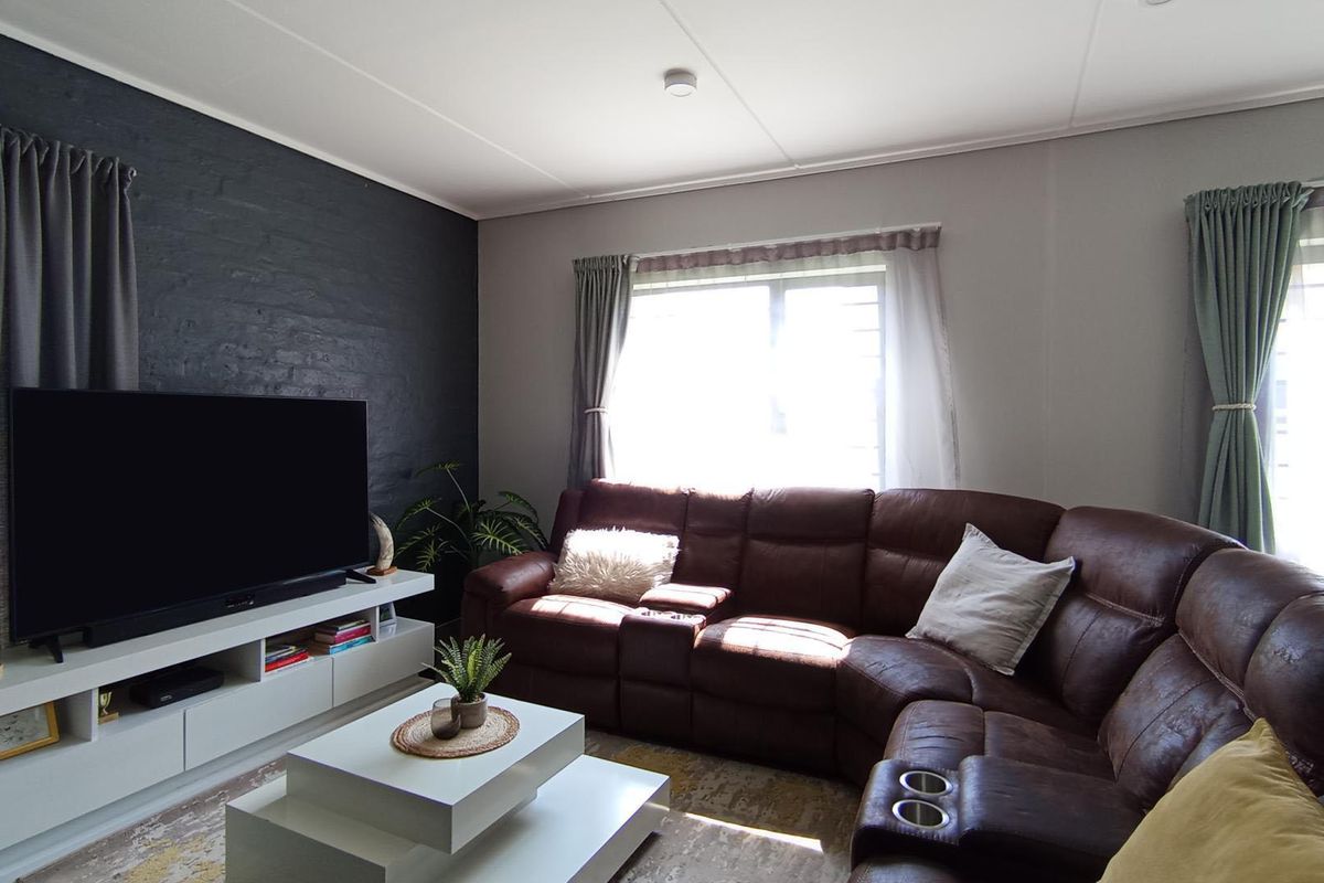 A well-maintained living room featuring a dark painted brick accent wall, built-in media cabinetry, and natural light through aluminium-framed windows.