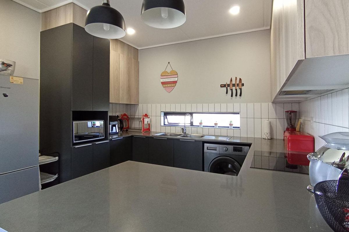 Modern kitchen featuring dark cabinetry, stone countertops, integrated appliances, and a tiled backsplash with a horizontal window for natural light.