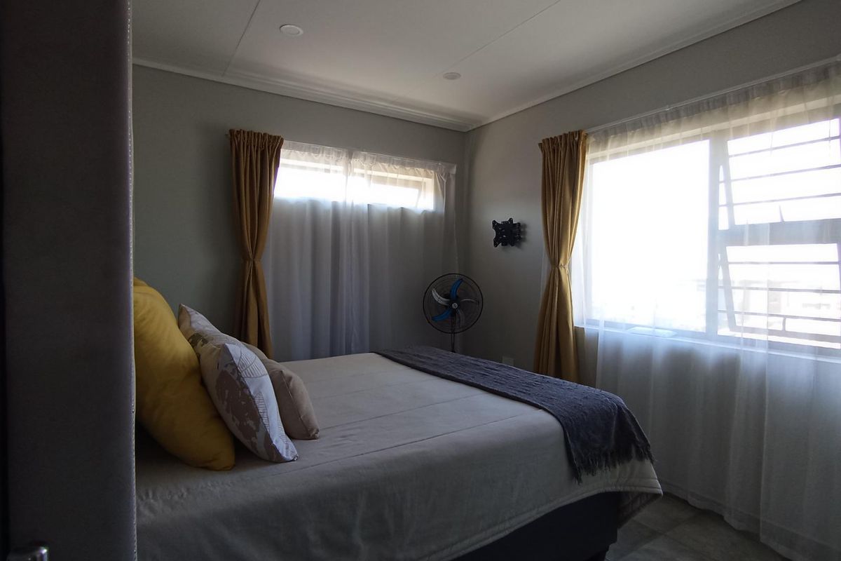 A well-lit bedroom featuring neutral wall tones, recessed ceiling lighting, and large windows that provide ample natural light.
