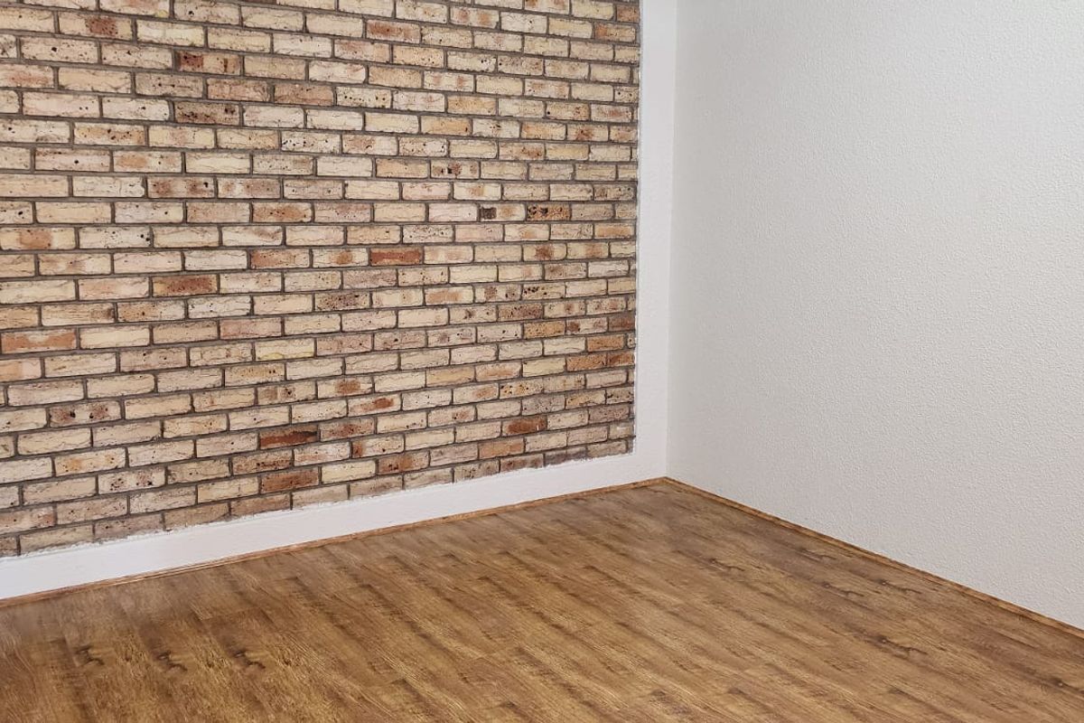 An empty bedroom featuring a rustic exposed brick accent wall and modern laminate wood-look flooring.
