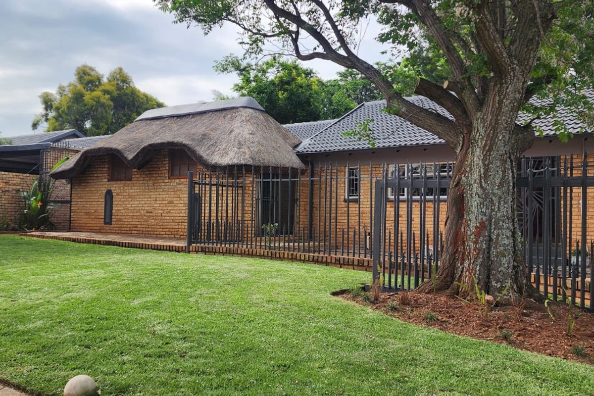 Rear view of the property featuring a combination of thatched and tiled roofing, face brick exterior, and secure metal fencing surrounding a lawn area.