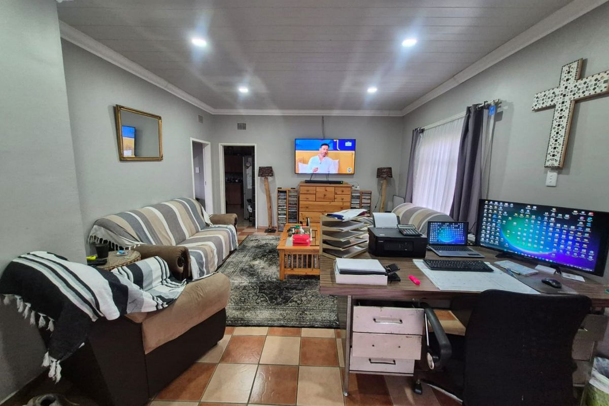 A functional living room featuring tiled flooring, recessed downlighting, and timber-look ceiling panels, currently utilized as a multi-purpose living and workspace area.