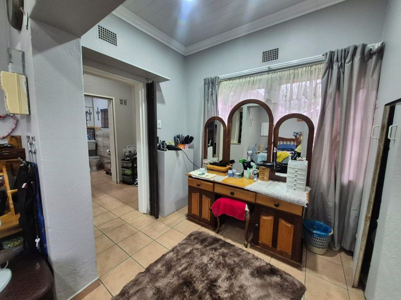 A bedroom featuring tiled flooring, ceiling cornices, and ventilation grilles, with an adjoining doorway leading to a bathroom area.