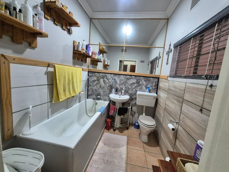 A functional bathroom featuring a bathtub, pedestal sink, toilet, and large wall mirror with tiled finishes throughout.