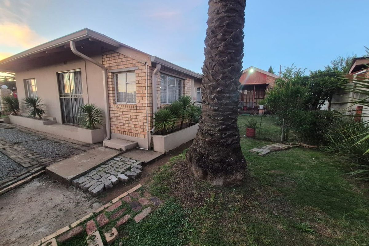 Rear view of a brick house featuring a garden area, concrete pathways, and established landscaping with security bars on windows.