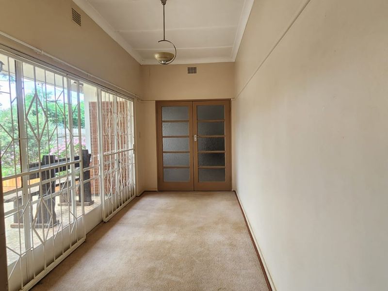 A spacious, empty hallway featuring carpet flooring, double doors, and large sliding glass doors with security gates leading to the exterior.