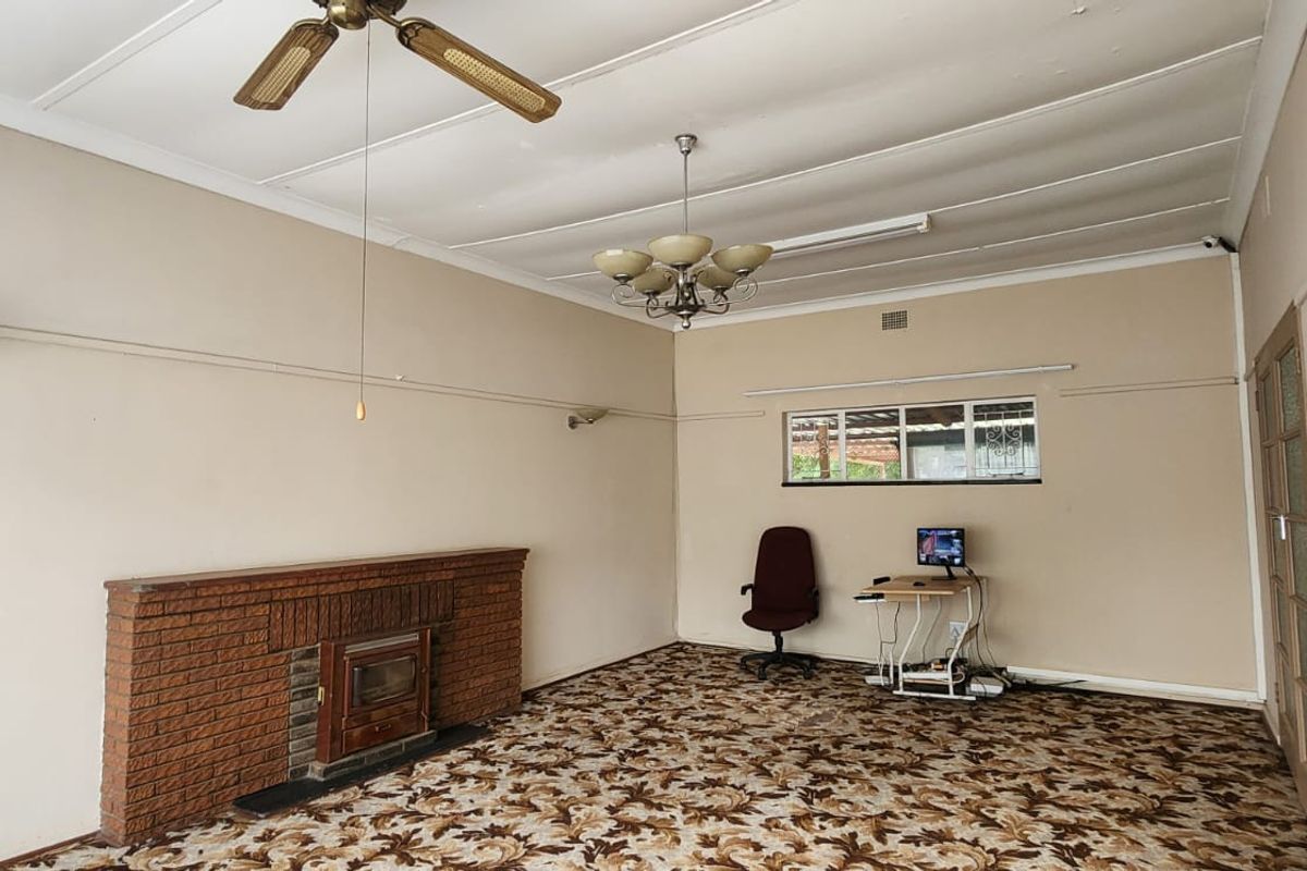 Spacious living room featuring a classic brick fireplace with a wood-burning stove insert, patterned carpeting, and traditional ceiling lighting fixtures.