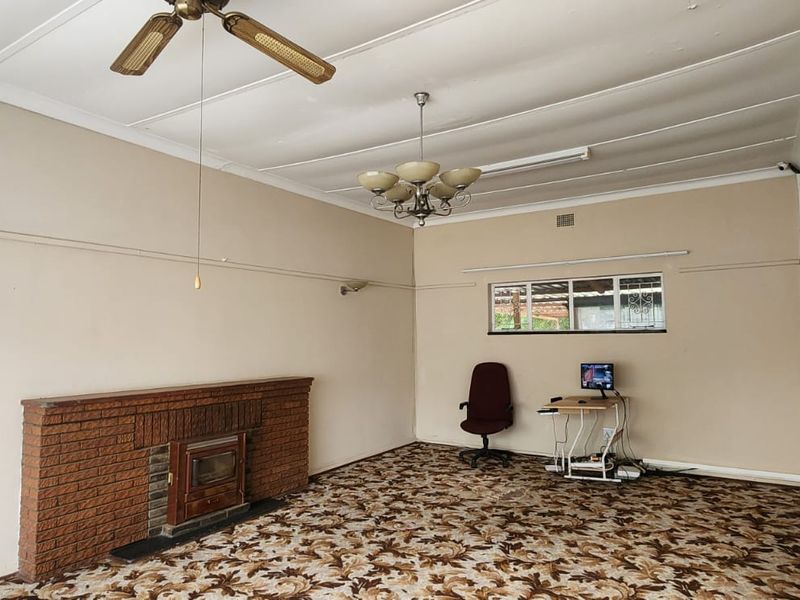 Spacious living room featuring a classic brick fireplace with a wood-burning stove insert, patterned carpeting, and traditional ceiling lighting fixtures.