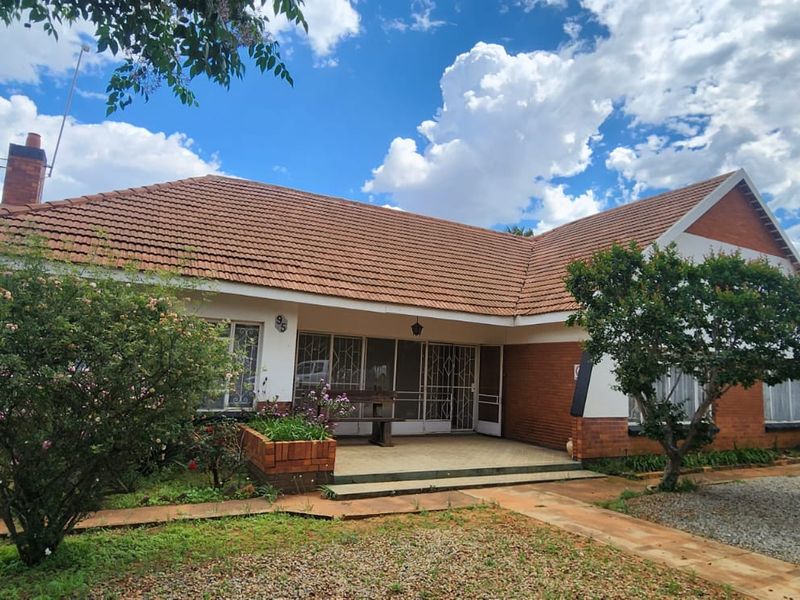 A charming single-story brick house featuring a tiled roof, a covered front patio, and a well-established garden with a brick planter box.