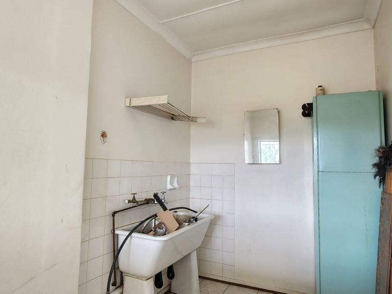 A functional laundry area featuring a traditional ceramic sink, tiled splashback, and built-in storage cupboard, offering potential for modernization.