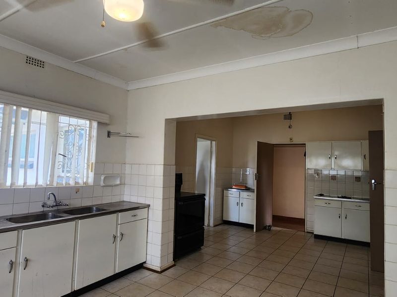 A dated kitchen featuring built-in cabinetry, a double basin sink, and tiled splashbacks, with visible ceiling water damage requiring attention.
