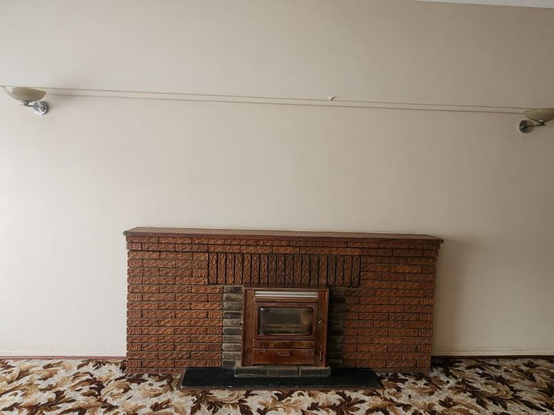 A spacious living room featuring a traditional brick fireplace with an integrated wood-burning stove and wall-mounted lighting fixtures.