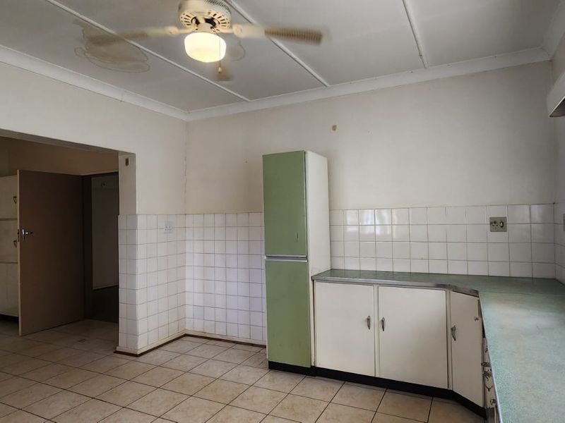 A spacious, dated kitchen featuring tiled flooring, ample built-in cabinetry, and laminate countertops, offering significant potential for a modern renovation.