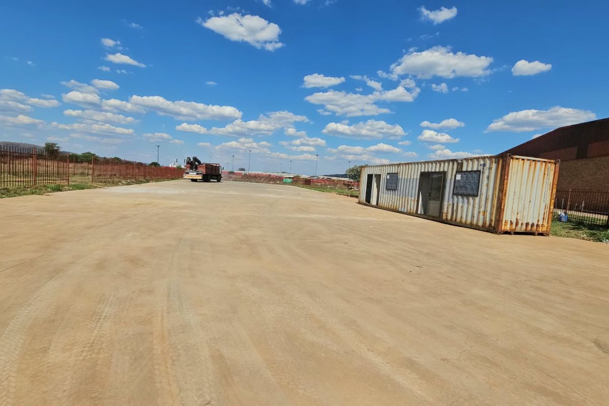Expansive vacant land area featuring concrete paving, perimeter steel fencing, and a shipping container structure suitable for site office or storage use.