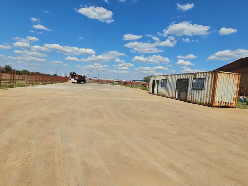 Expansive vacant land area featuring concrete paving, perimeter steel fencing, and a shipping container structure suitable for site office or storage use.