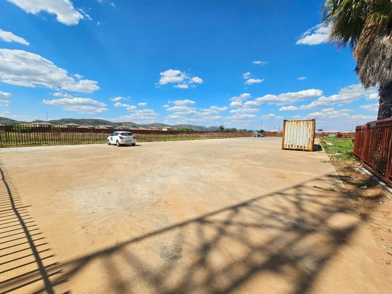 A large, level vacant residential plot featuring a concrete hardstand surface and secure perimeter steel fencing, suitable for development.