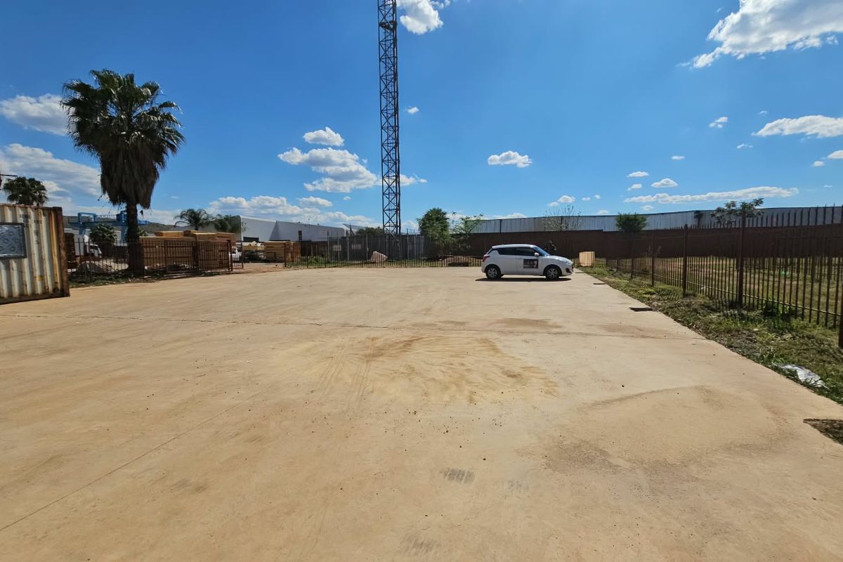 A wide-angle view of a vacant residential land plot featuring extensive concrete paving, perimeter metal fencing, and a shipping container structure.