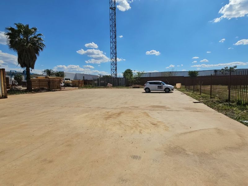 A wide-angle view of a vacant residential land plot featuring extensive concrete paving, perimeter metal fencing, and a shipping container structure.